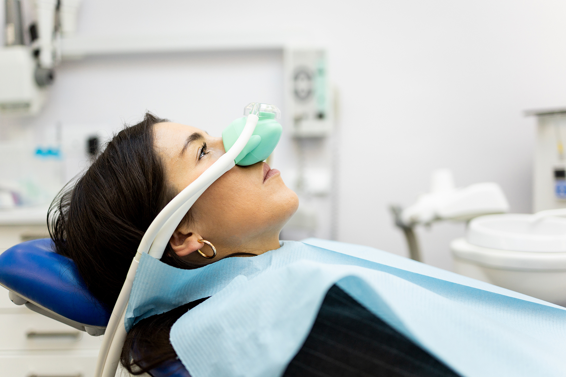 The image shows a person sitting in a dental chair with an oxygen mask on their face, receiving dental treatment in a dental office setting.